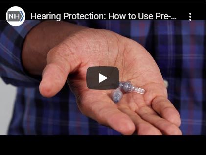 A screenshot of video depicting an adult hand holding pre-molded earplugs.