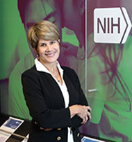 An image of Dr. Tucci standing in a hallway next to a sign that reads, 'NIH National Institute on Deafness and Other Communication Disorders.'