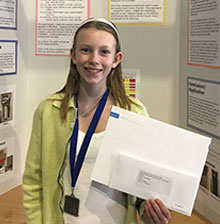 13-year-old Nora Keegan stands in front of a poster presentation detailing her research.