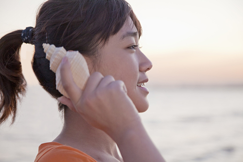 A woman holding a seashell next to her ear to hear the sound