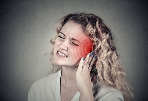 A young woman holds her ear while grimacing in pain.