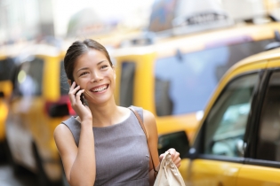 Business woman on smart phone in New York City, Manhattan walking in dress suit holding doggy bag smiling and laughing, Young multiracial Asian Caucasian professional female businesswoman in her 20s.