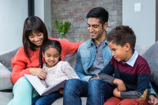 Family sitting around reading a book. 