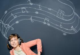 Young girl wearing a personal music device. She is standing in front of a blackboard that has musical notes written in chalk.